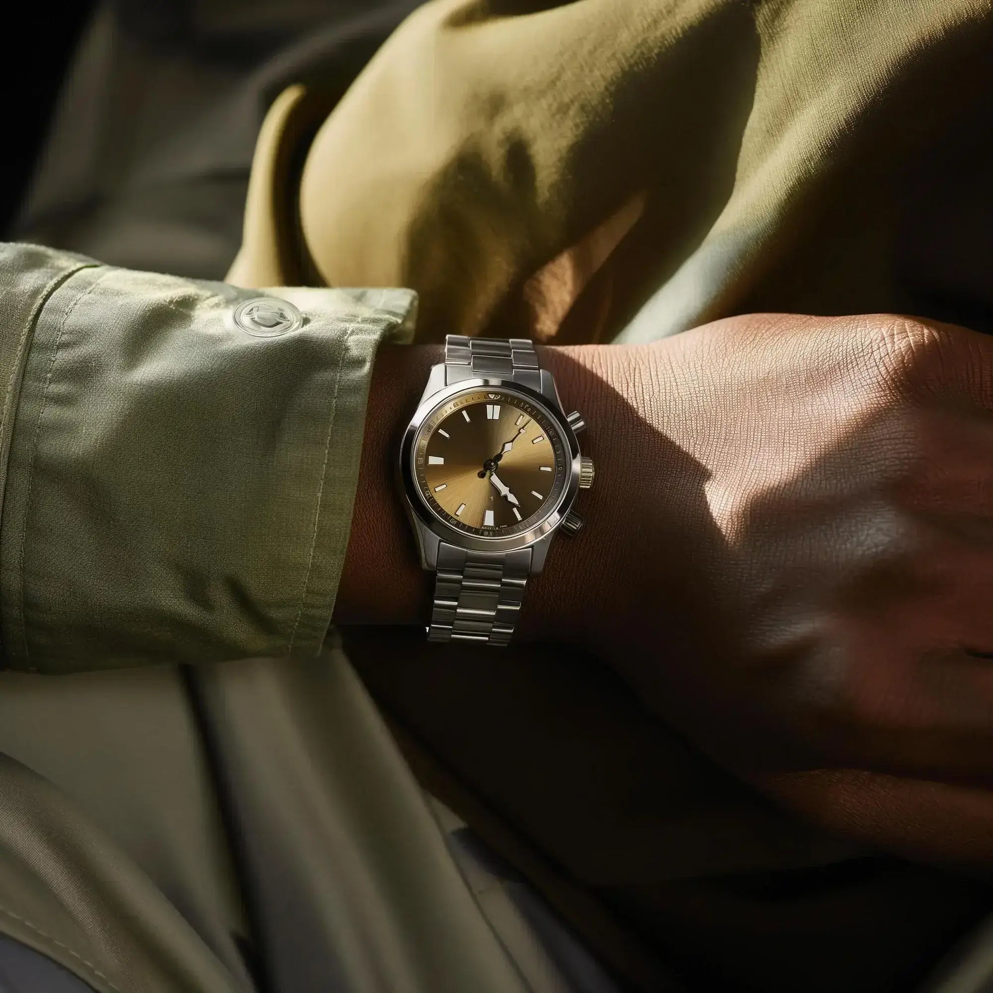 Close-up of a wrist wearing a silver watch with a gold face, against a blurred background.